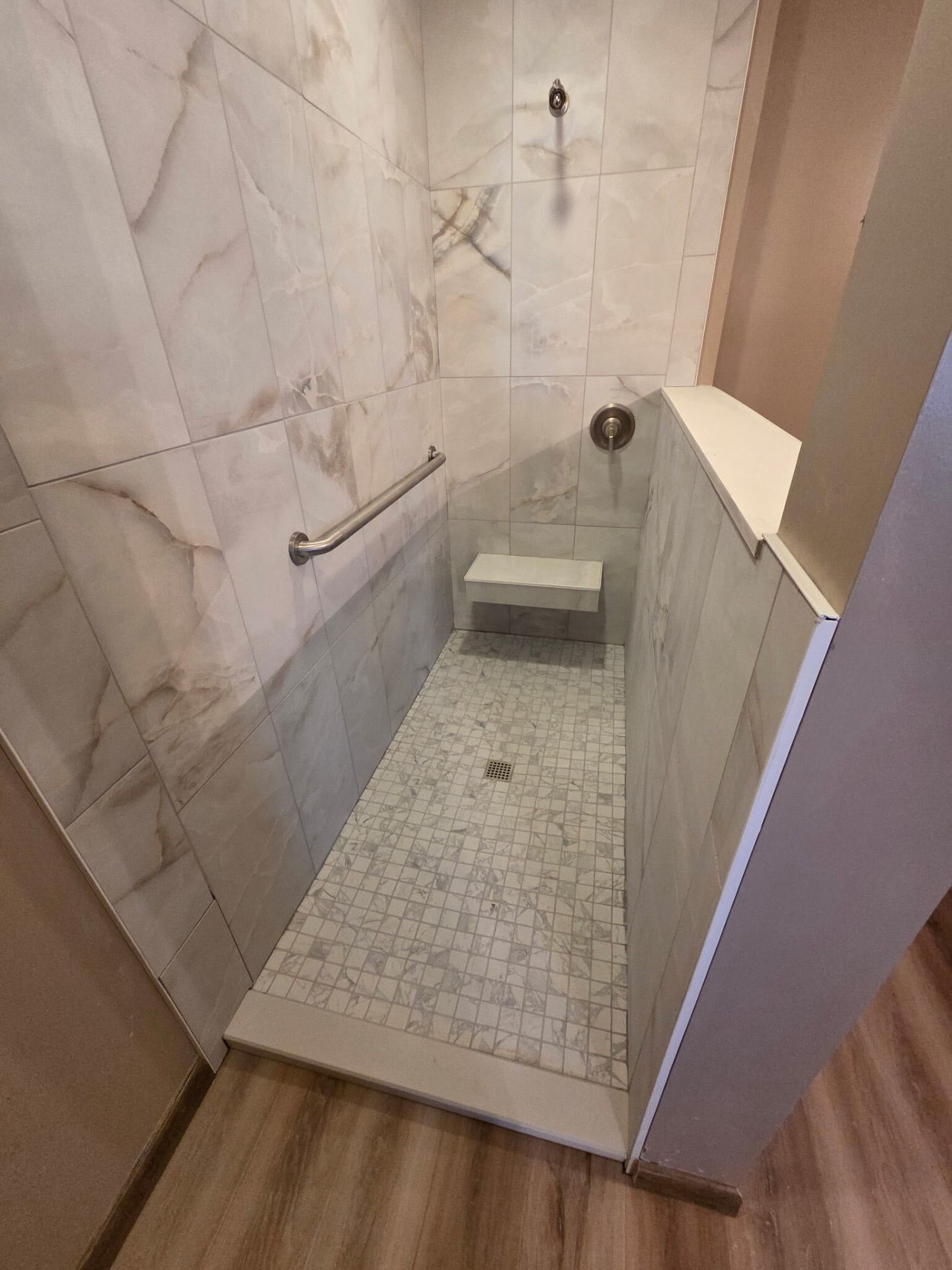 Walk-in marble tile shower with built-in bench and mosaic floor